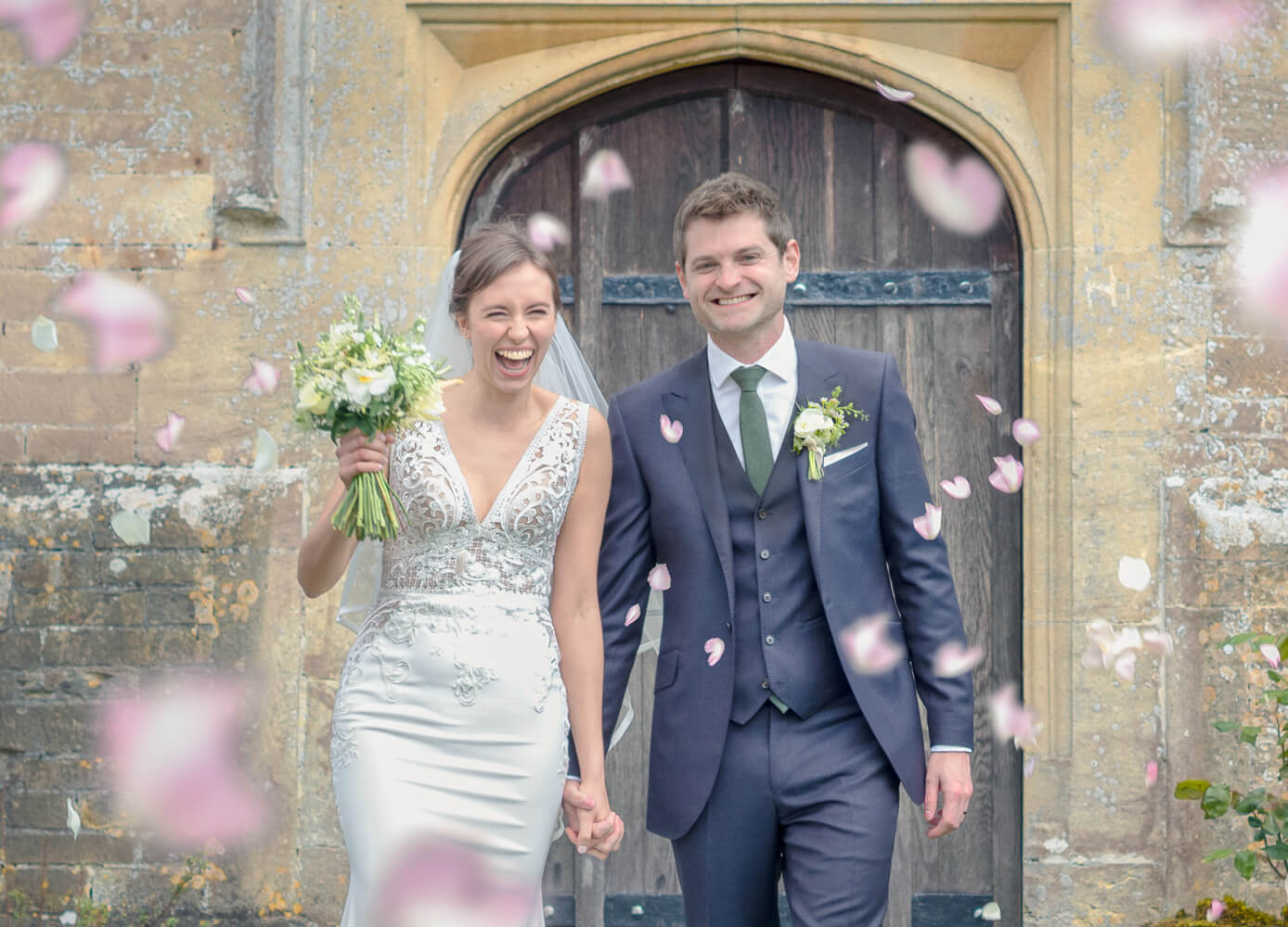 Newly weds with pink confetti outside church doors laughing and smiling